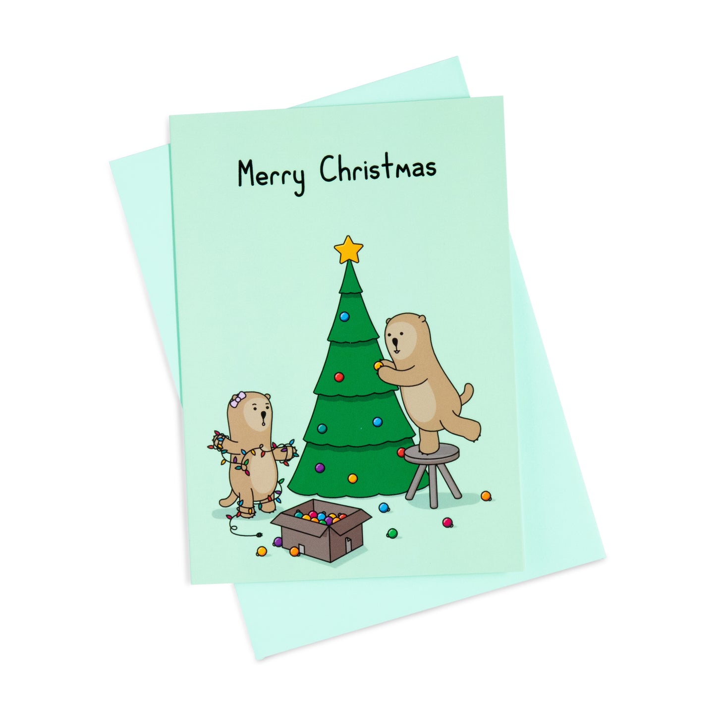 A green Christmas greeting card with a cheerful illustration of two otters decorating a Christmas tree. One is reaching to put decorations on the tree, the other is tangled in Christmas lights. The text on the card reads 'Merry Christmas'.