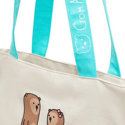 A canvas tote bag with aqua coloured handles and aqua lining. Two otters are shown holding hands on both sides.