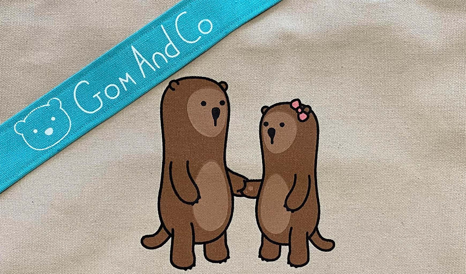 A closeup of the otter image printed on the canvas tote bag. The aqua handle with logo is shown across the top left corner.